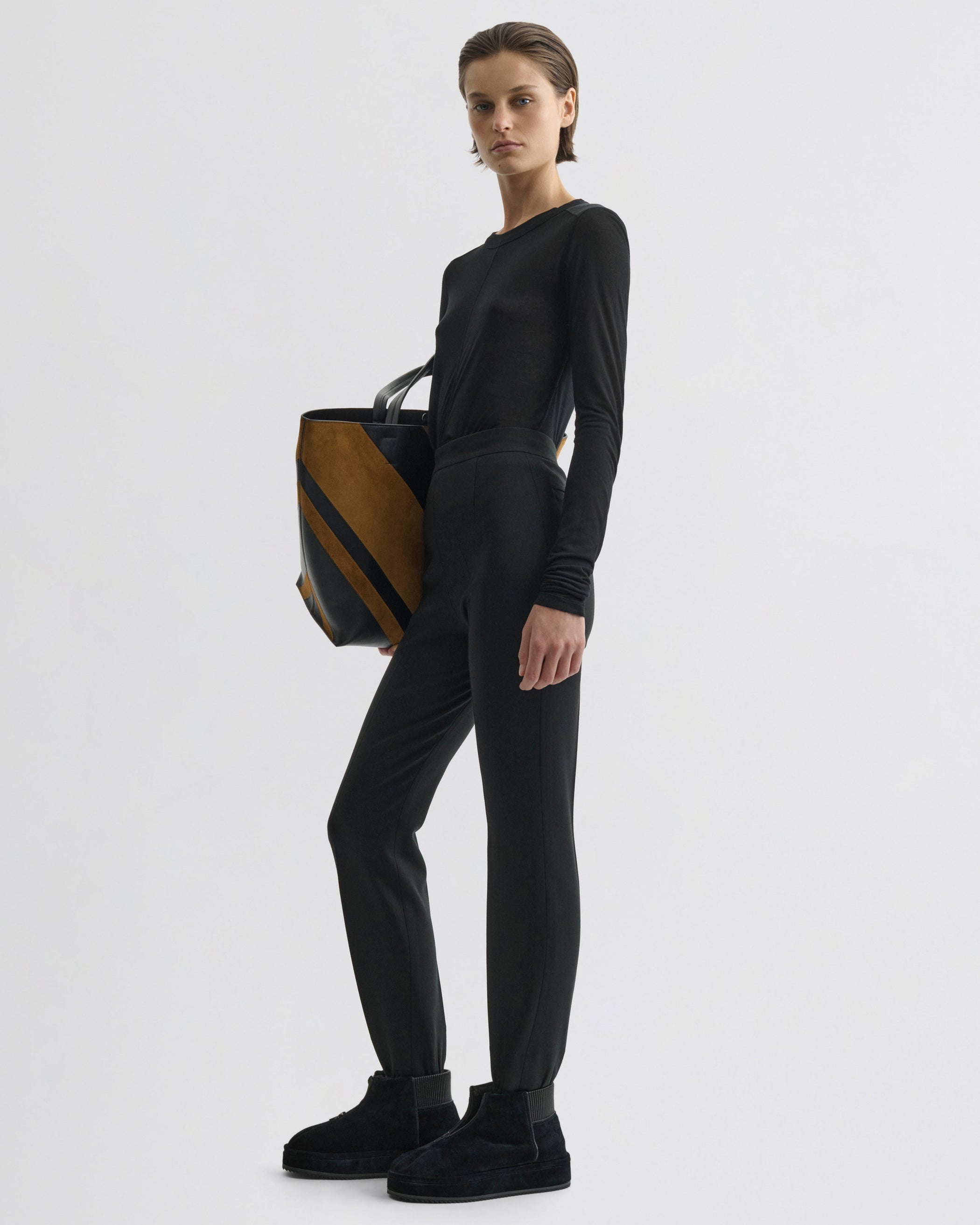 Side view of model wearing Stirrup Trousers in black wool