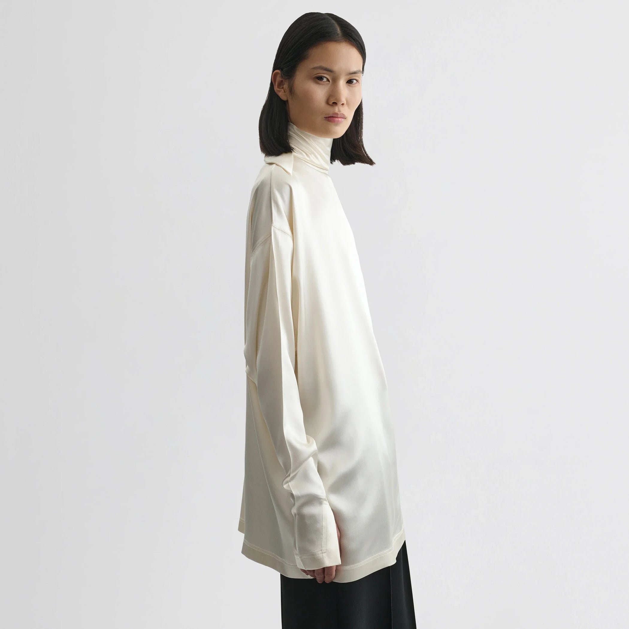 Side view of model wearing liquid knot collar top in cream silk.