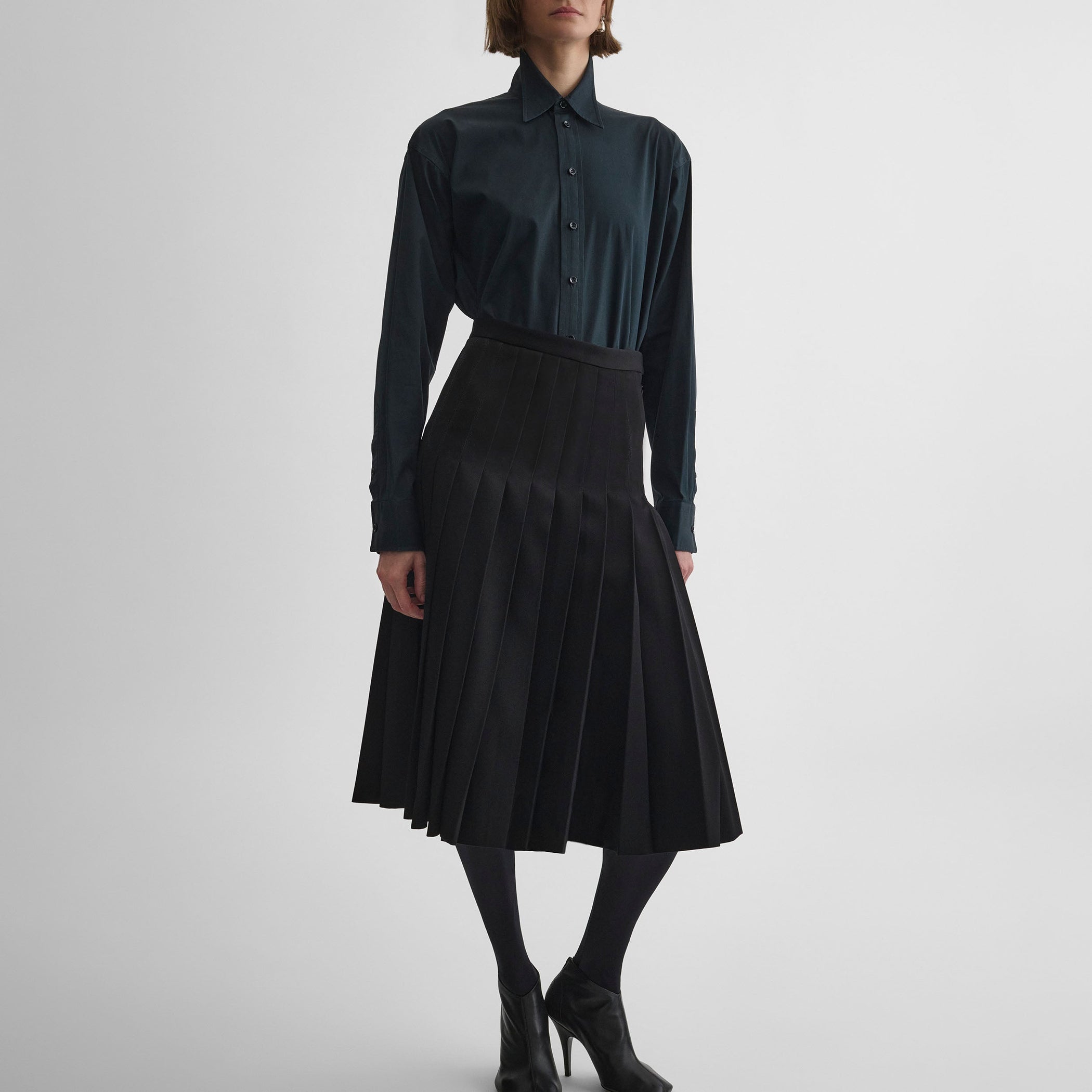 Front view of model wearing UNIFORM PLEATED SKIRT in black wool blend