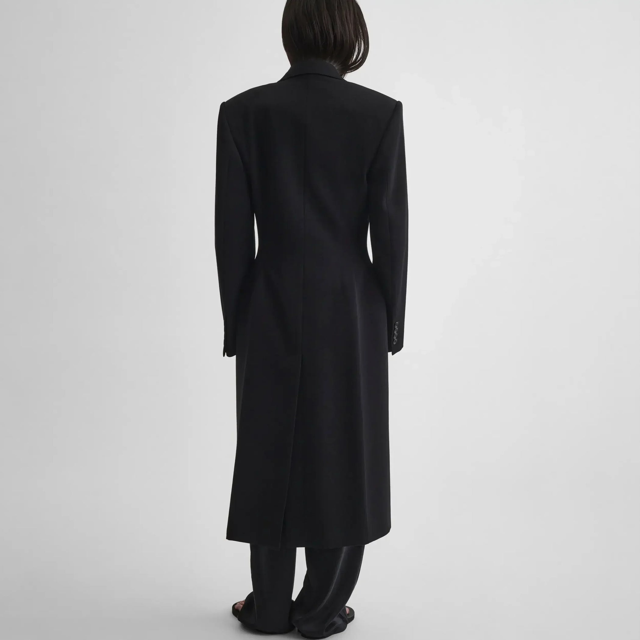 Back view of model wearing TAILORED COAT WITH DROPPED WAIST in black wool