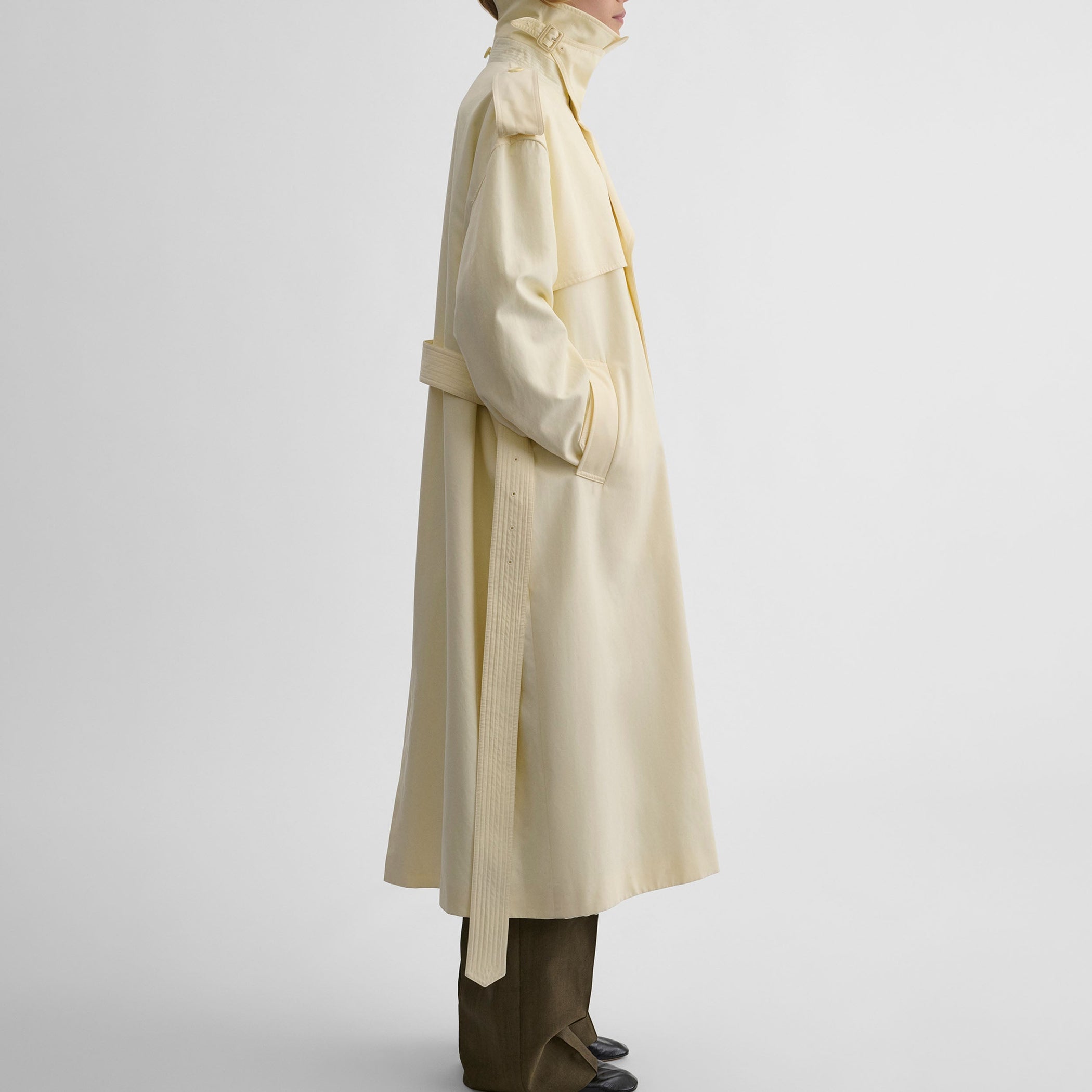 Side view of model wearing TRENCH COAT WITH ATTACHABLE SCARF in cream technical polyester
