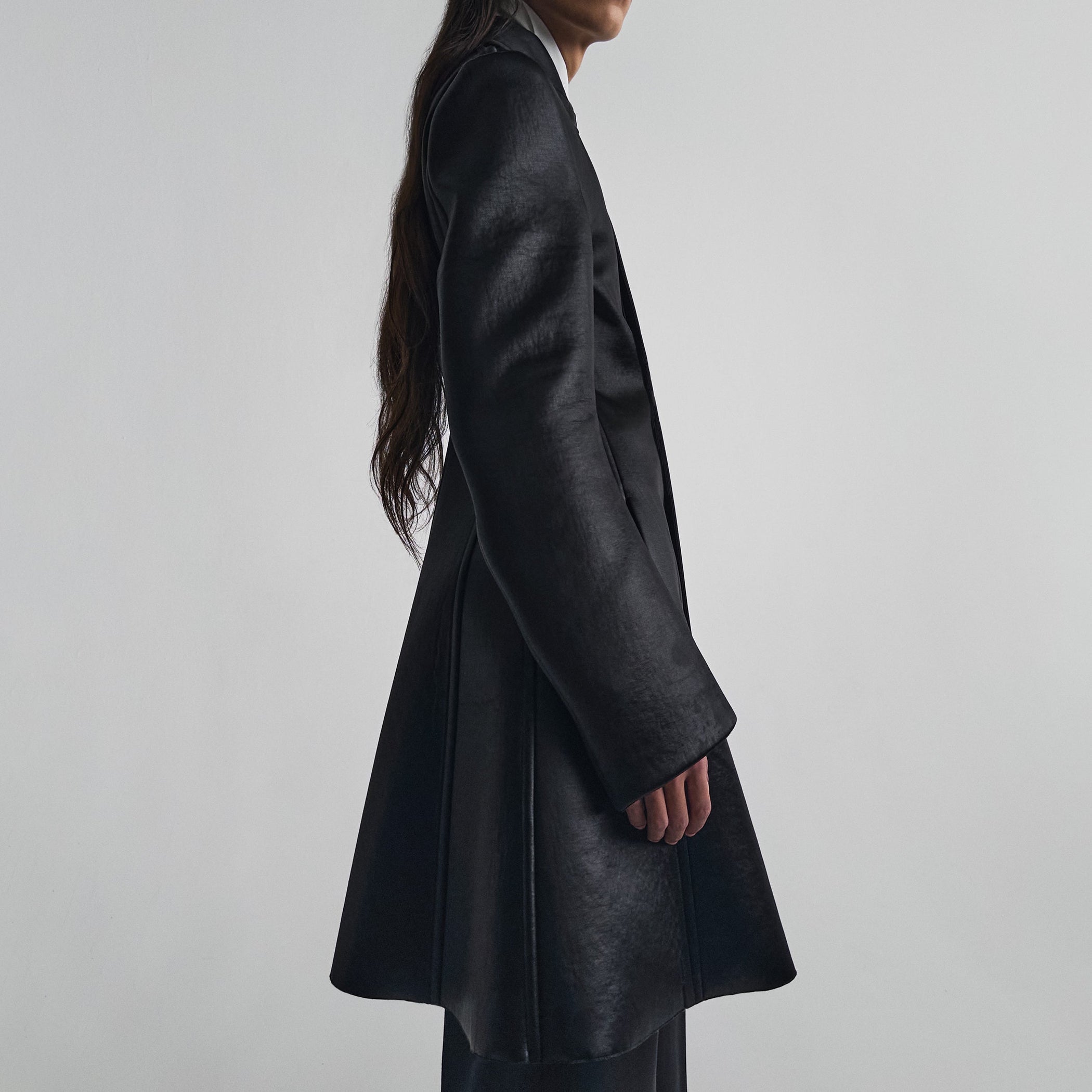 Side view of model wearing SHORT COAT in black bonded satin