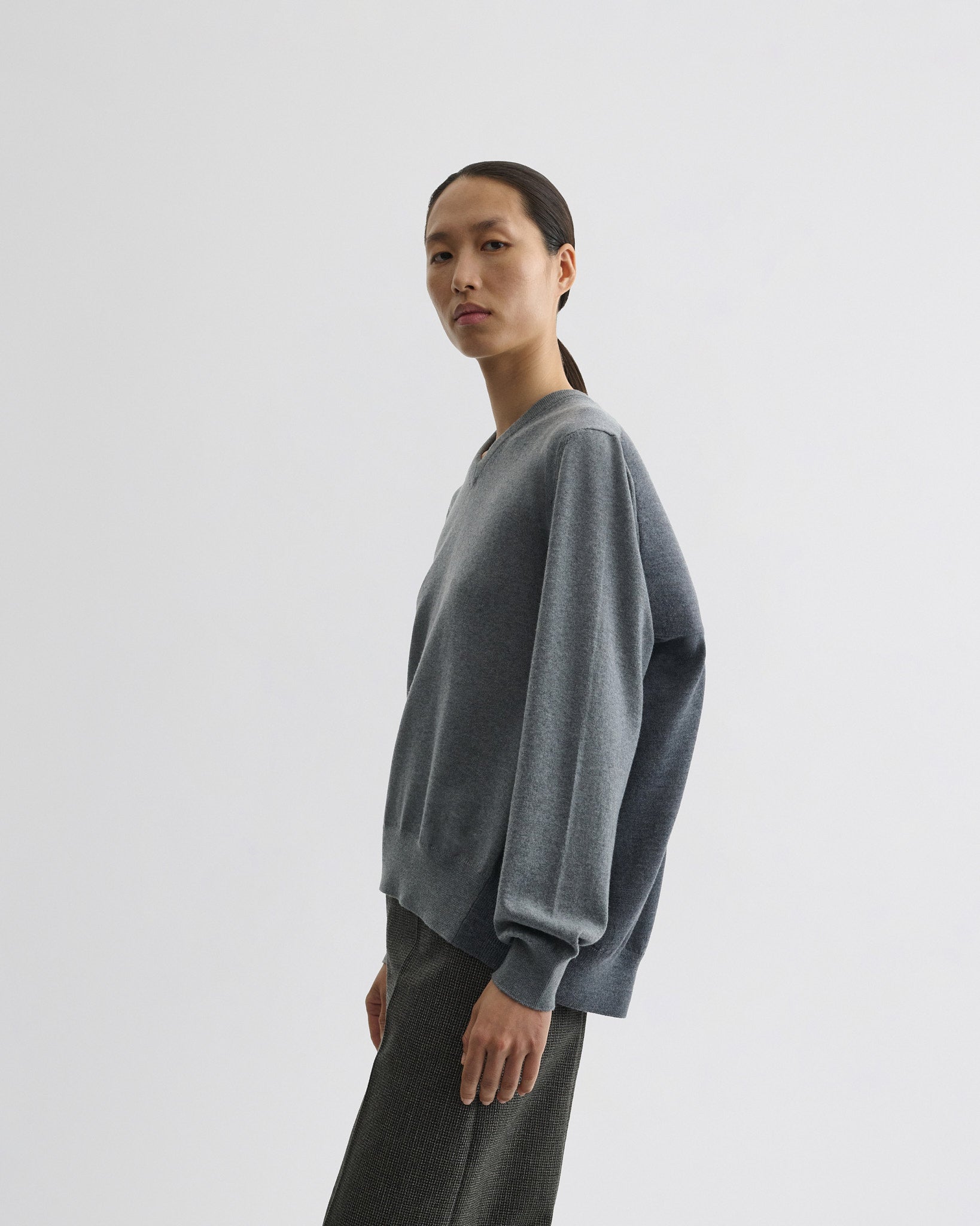 Side view of model wearing backed v-neck sweater in light grey wool.