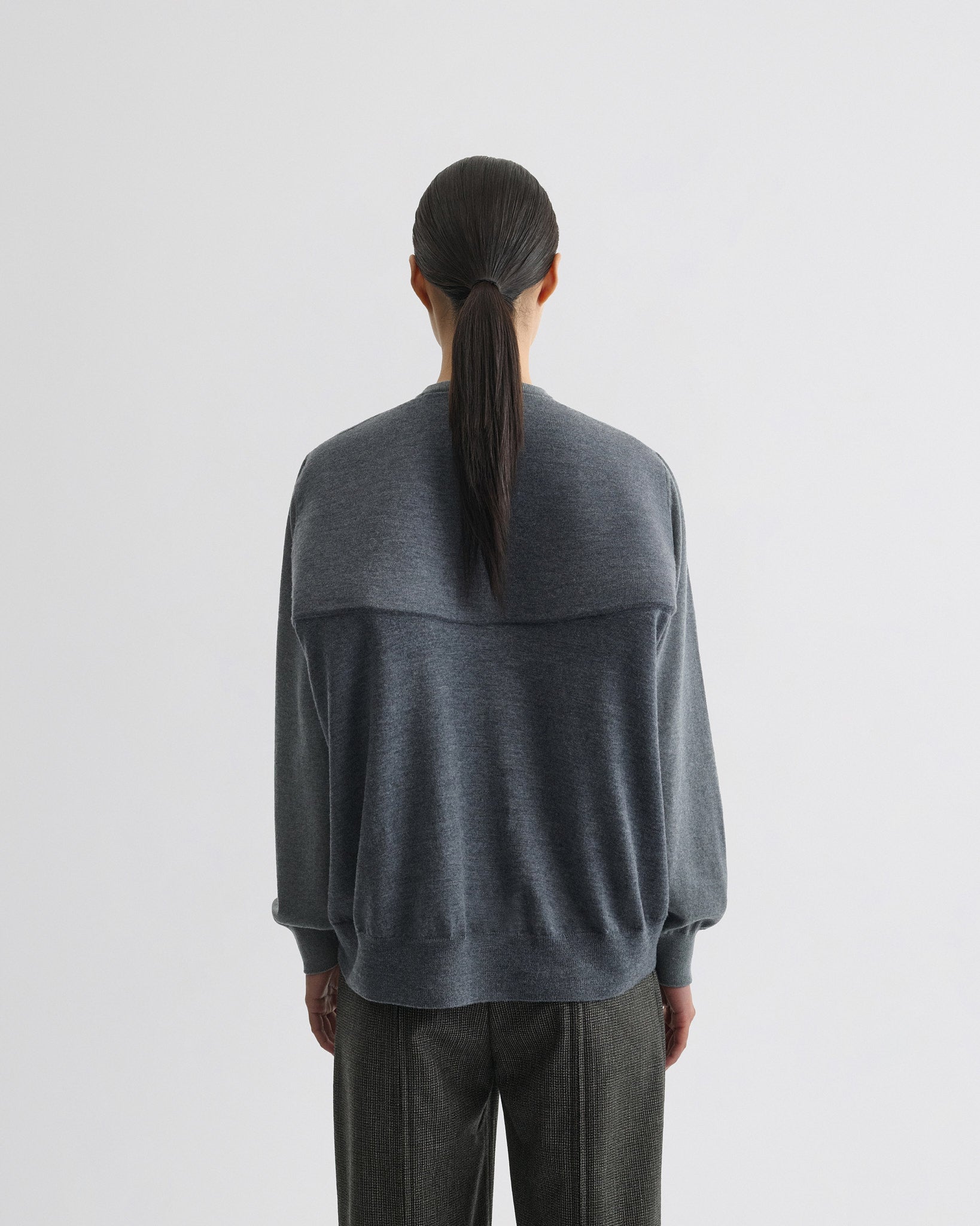 Back view of model wearing backed v-neck sweater in light grey wool.