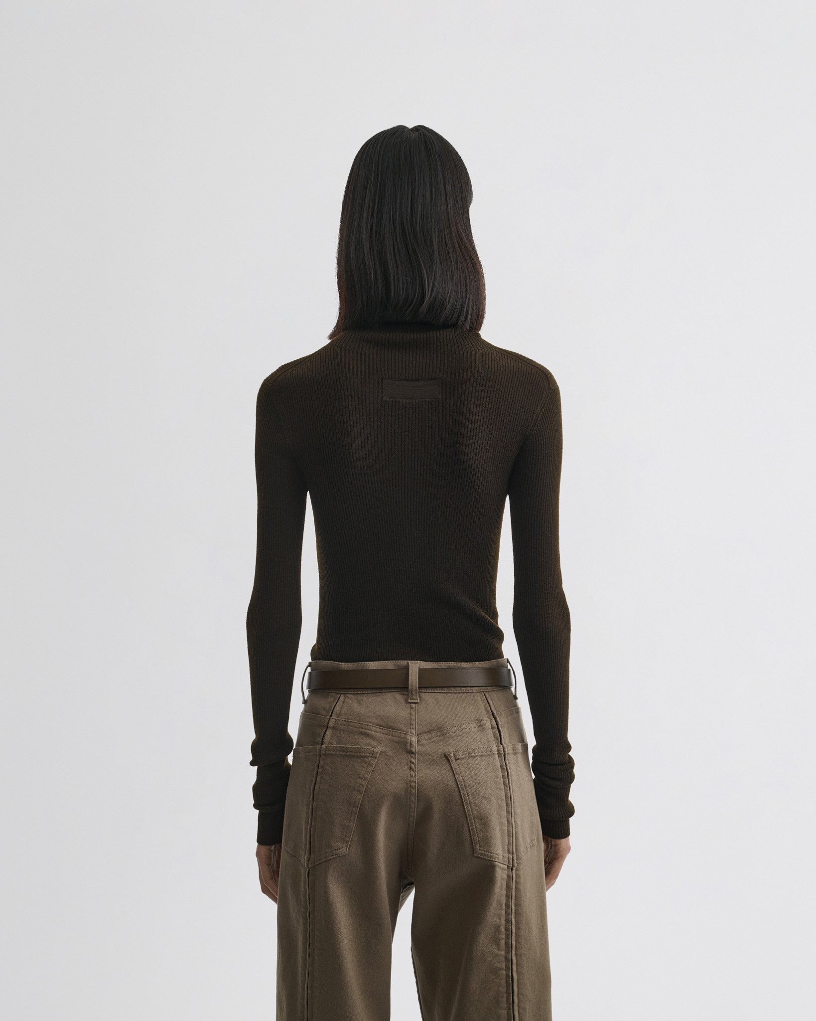 Back view of model wearing fine rib high neck top in dark khaki wool.