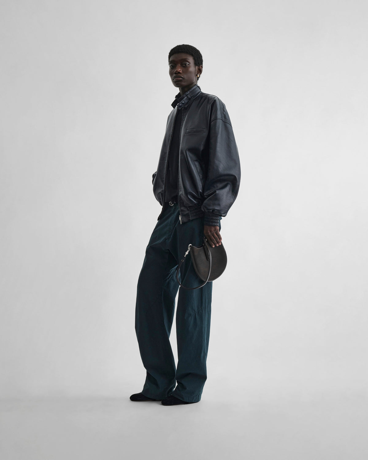Front view of model holding MINI BEAN SLING in chocolate brown leather