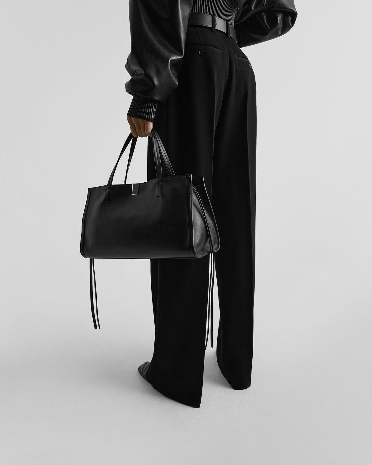Side view of model holding SMALL KIT CABAS in black leather