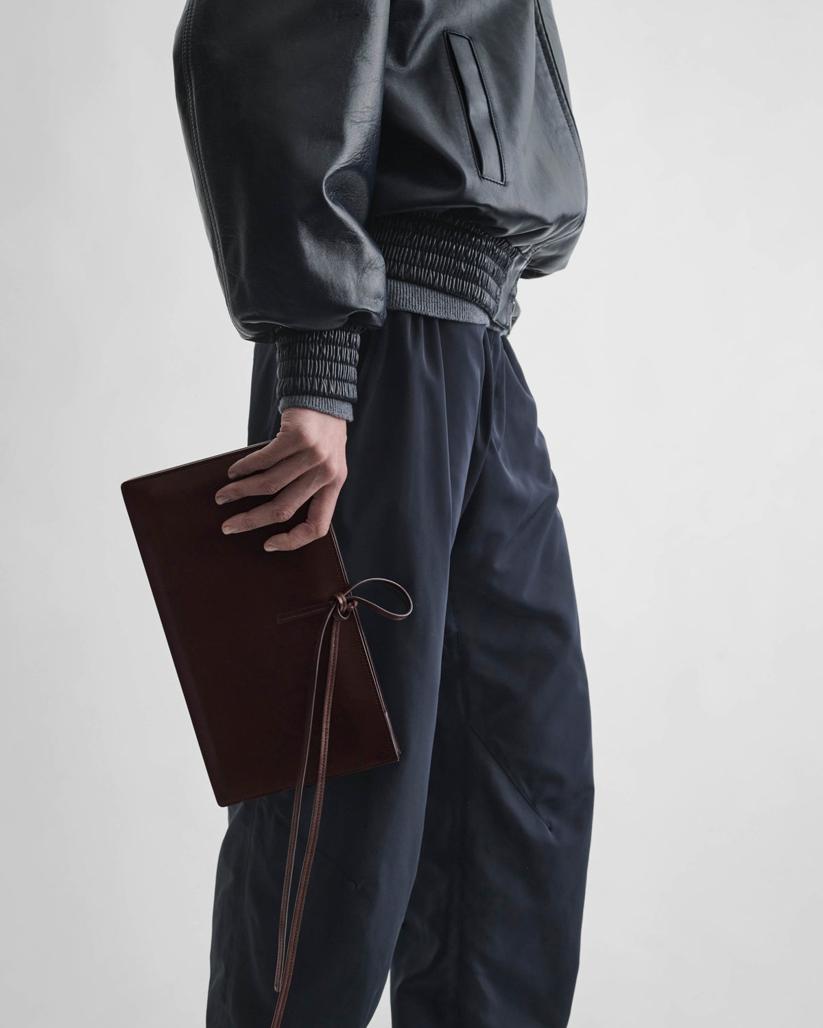 Side view of model wearing SPLAY CLUTCH in bitter chocolate leather